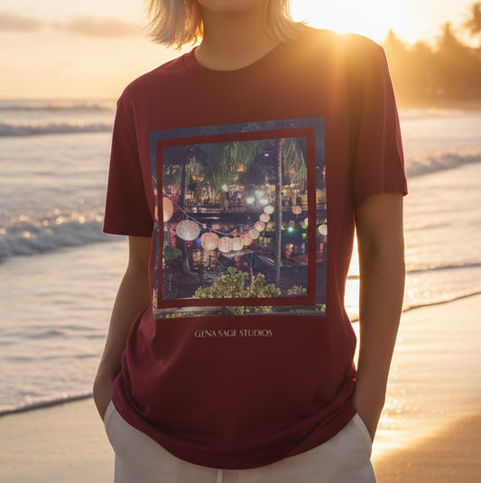 Model wearing Tropical Lantern Nights Art Tee by Gena Sage Studios featuring framed evening lantern market photograph on burgundy shirt at sunset beach 